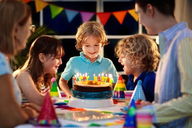 Kids birthday party. A child blows out the candles on the cake and opens the presents. Celebrating the pastel rainbow theme. Family celebrating at home. A boy opens gifts and eats cake. Come to the party using the Black Car Service.